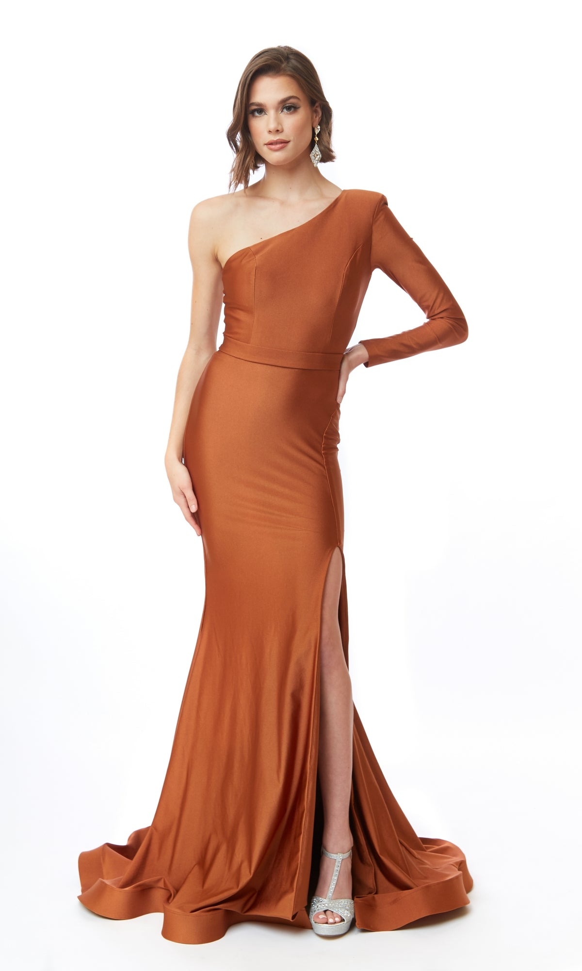 A woman poses in the Atria 6716H One-Sleeve Long Prom Dress with train and side slit, featuring a copper hue and floor-length hem, standing against a plain white background.